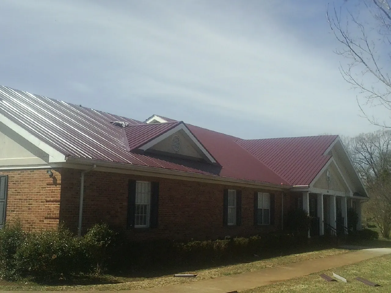 Red metal roof with gabled entries on a long brick building, from a Hail Damage Roof Repair job in Mc Arthur