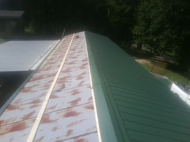 Old rusted panels beside newly installed green metal roofing — Wind Damage Roof Repair by Roofing Brothers in Mc Arthur