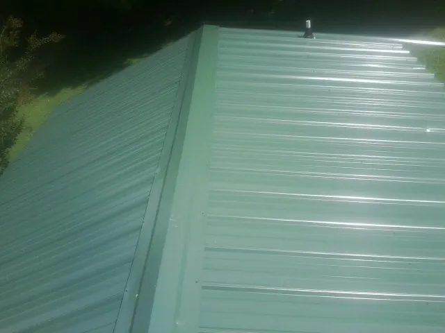New green metal panels meeting at the ridge of a roof — Flat Roof Repair work by our crew in Mc Arthur
