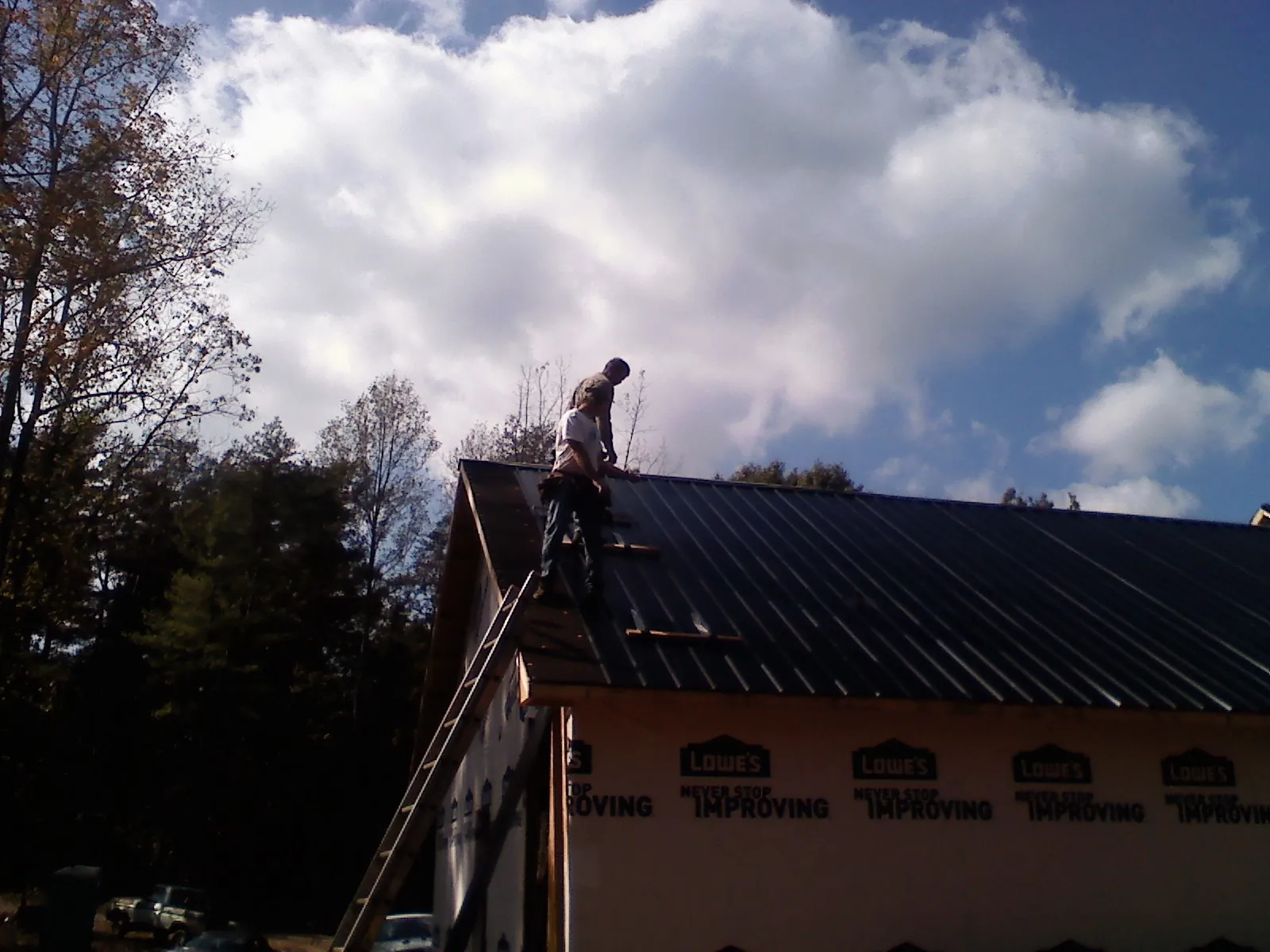 Roofer fastening dark metal panels high against a cloudy sky, from a Roof Inspection job in Mc Arthur