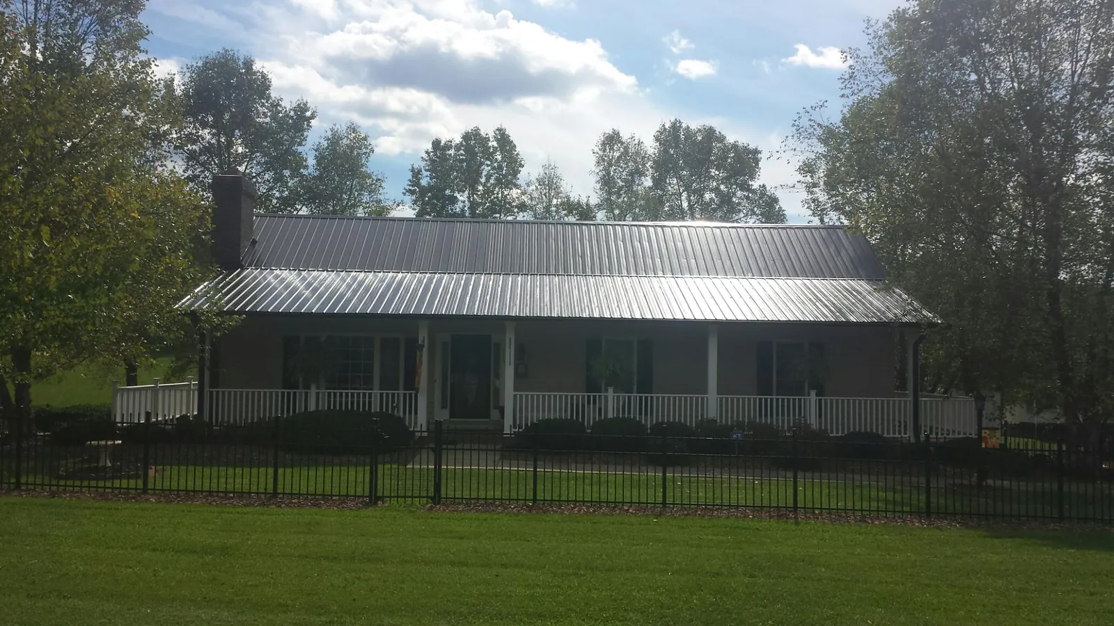 Gray metal roof on a brick ranch with a full width front porch — Gutter Guard Installation work by our crew in Mc Arthur